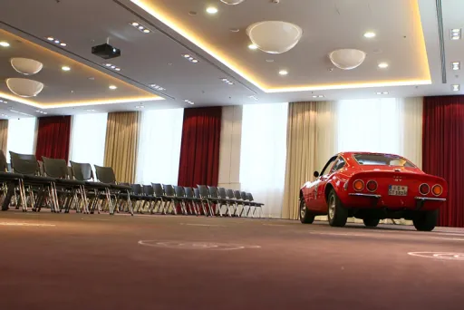 Roter Oldtimer steht in einem modernen, leeren Konferenzraum mit Stuhlreihen.