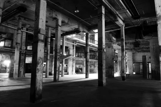 Schwarzweißfoto einer leeren, verlassenen Industriehalle mit vielen Säulen.