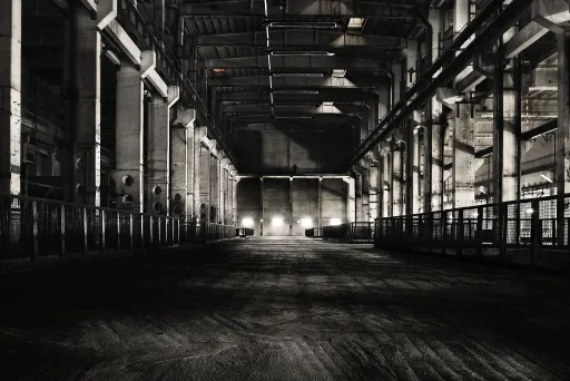 Dunkle, leere Industriehalle mit Licht am Ende des Gebäudes.