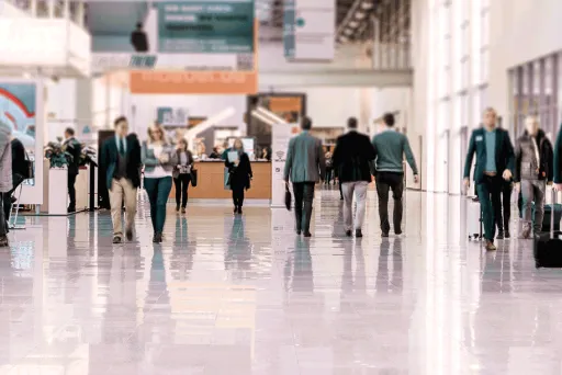 Menschen gehen durch eine helle, moderne Halle mit Glasfronten und glänzendem Boden.