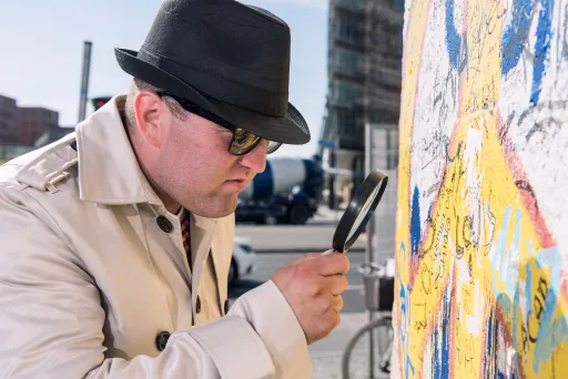 Meeting Guide Berlin Teamgeist Inspektor mit Lupe untersucht Mauerstück