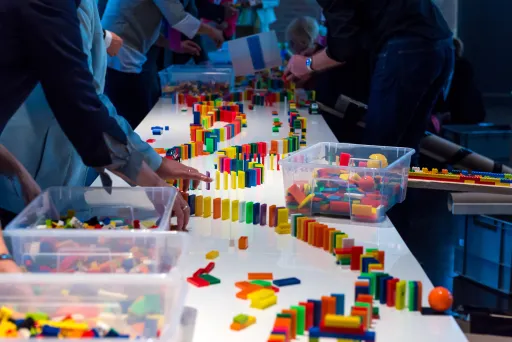 Meeting Guide Berlin Teamgeist Team baut eine Dominoreihe auf einem Tisch