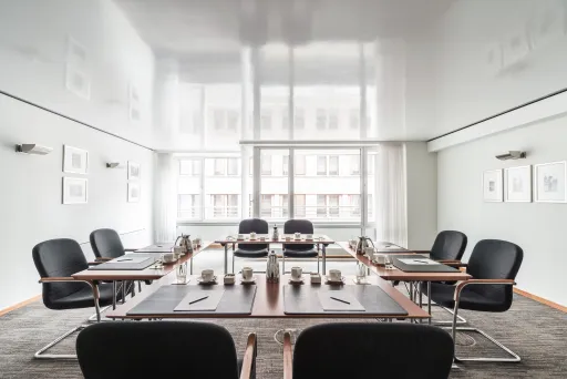 Moderner Konferenzraum mit schwarzem Stuhlkreis und großem Fenster im Hintergrund.