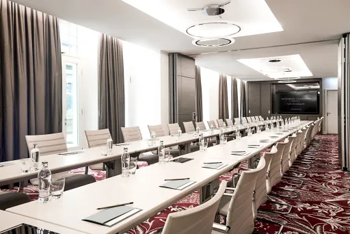 Konferenzraum mit langen Tischen, weißen Stühlen und moderner Beleuchtung