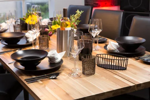 Modern gedeckter Esstisch mit schwarzem Geschirr und Blumen als Dekoration.