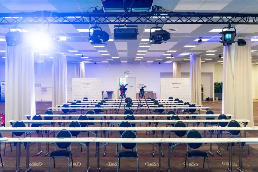 Leerer Konferenzraum mit Reihenstühlen, Bühne und Kameraleuten.