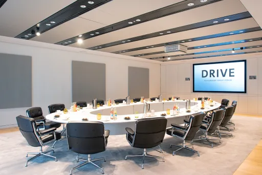 Moderner Konferenzraum mit rundem Tisch, schwarzen Stühlen und großem Bildschirm