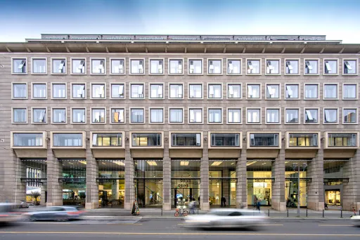 Modernes Bürogebäude mit Glasfassade und vorbeifahrenden Autos auf der Straße.