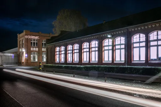 Beleuchtetes Backsteingebäude bei Nacht mit Lichtspuren auf der Straße.