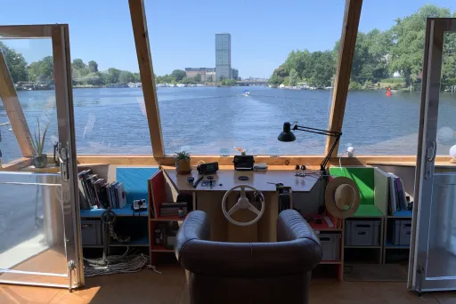 Steuerstand eines Bootes mit Ausblick auf einen Fluss und einen fernen Turm bei Sonnenschein.