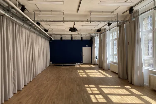 Heller Raum mit Holzfußboden, weißen Vorhängen und Sonnenlicht durch große Fenster.