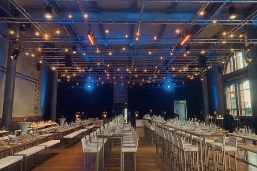 Festlich gedeckter Saal mit langen Tischen, dekoriert mit Lichterketten.