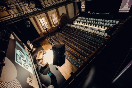 Leerer Veranstaltungssaal mit Bühne, Sesseln und Reihen von Stühlen.