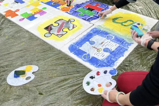Mehrere Personen bemalen gemeinsam ein großes Puzzle-Bild mit bunten Farben.