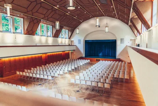 Festsaal Blick von der Empore in den Saal mit Reihenbestuhlung und Bühne mit blauem Vorhang