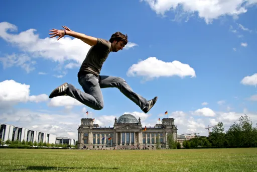 Mann springt vor dem Reichstagsgebäude in Berlin, blauer Himmel mit Wolken.