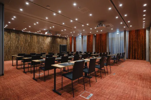 Konferenzraum mit mehreren Tischen und schwarzen Stühlen, warm beleuchtet.