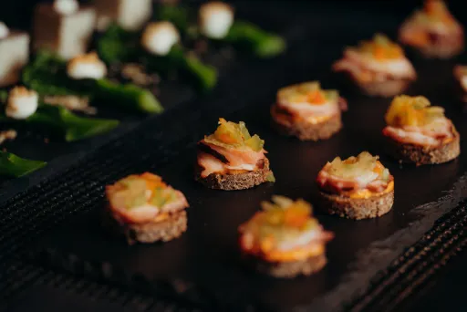 Kleine Canapés mit verschiedenem Belag auf einer schwarzen Servierplatte.