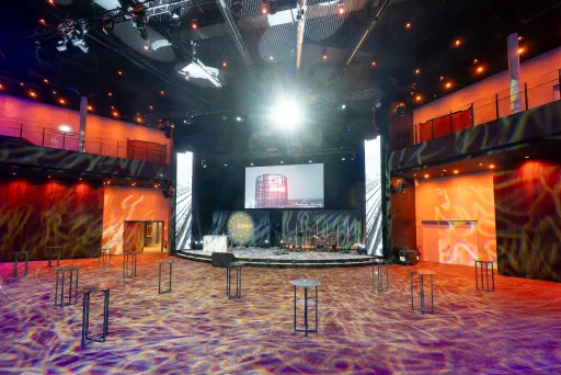 Großer, leerer Veranstaltungssaal mit Bühne und bunter Beleuchtung.