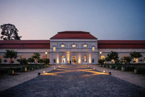 Beleuchtetes barockes Gebäude mit rotem Dach und symmetrischem Vorplatz bei Dämmerung.