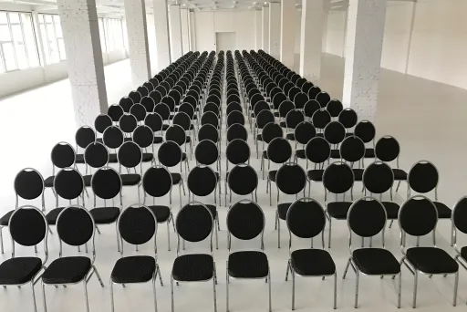 Viele Reihen schwarzer Stühle in einem großen, hellen Saal.