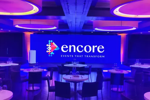 Modern eingerichteter Konferenzraum mit runden Tischen und lila-blauer Beleuchtung.