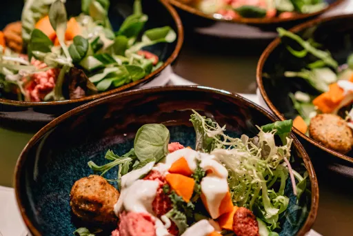 Mehrere Schalen mit bunter Gemüsesalat und Falafel auf einem Tisch.