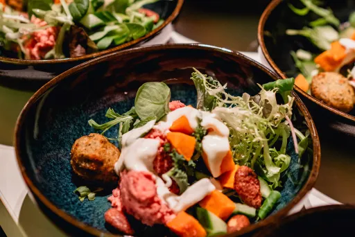 Mehrere Schalen mit bunter Gemüsesalat und Falafel auf einem Tisch.