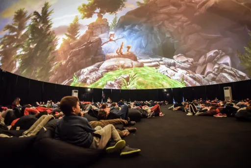 Menschen liegen auf Sitzsäcken und schauen eine Projektion in einer Kuppel an.