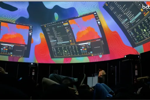 Menschen liegen in einem Kuppelraum, auf die Decke werden bunte Grafiken projiziert.