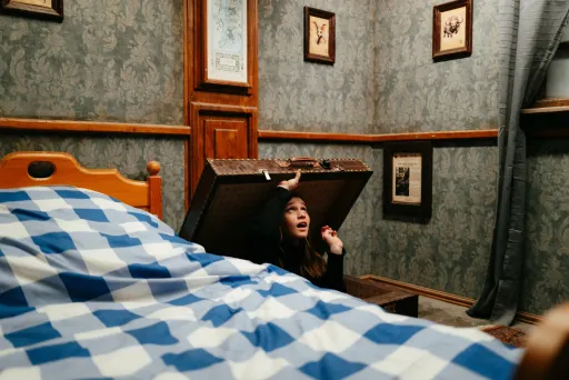 Frau öffnet versteckte Falltür in gemütlichem Schlafzimmer mit kariertem Bett.