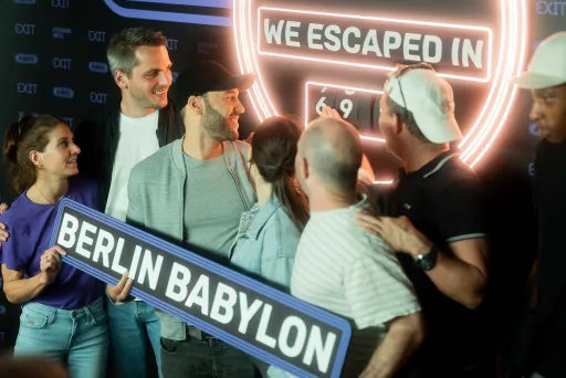 Gruppe jubelt vor Escape Room Schild, hält „Berlin Babylon“ Schild.