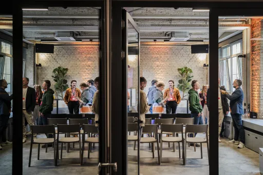 Menschen unterhalten sich stehend in modernem Konferenzraum mit Stühlen und Pflanzen.