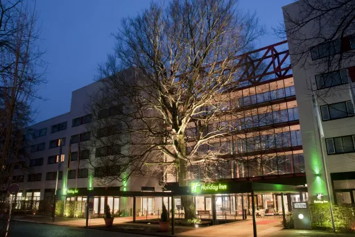 Modern hotel exterior with large lit tree and glass entrance at dusk.