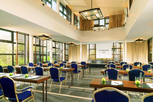 Heller Konferenzraum mit blauen Stühlen, Tischen und großem Fenster.