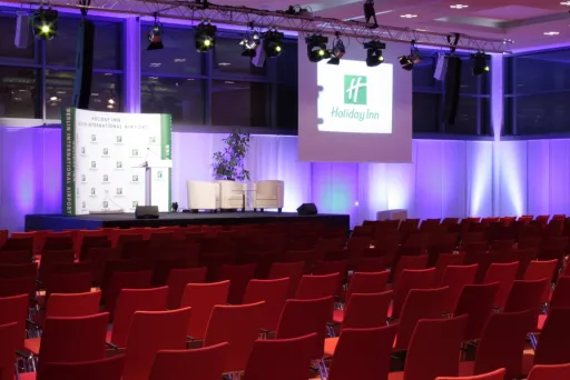 Leerer Konferenzraum mit roten Stühlen und beleuchteter Bühne, Holiday Inn Logo auf Leinwand.
