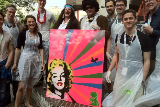 Gruppe von Menschen mit buntem Pop-Art-Gemälde, alle tragen weiße Schutzschürzen.