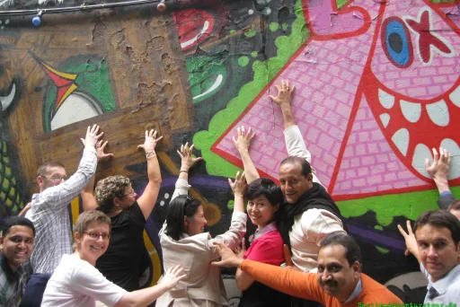 Gruppe fröhlicher Menschen posiert vor bunter Graffiti-Wand.