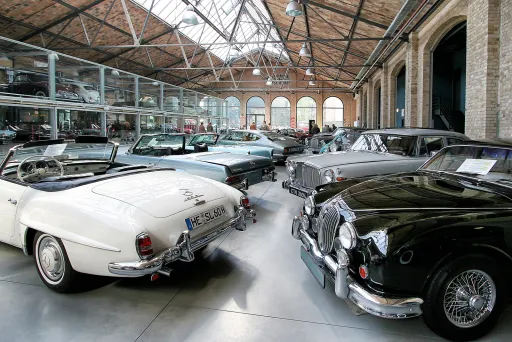 Klassische Oldtimer stehen in einer hellen, historischen Ausstellungshalle.