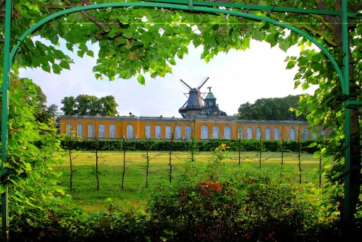 Green archway frames a windmill atop a yellow building, with grass and trees in front.