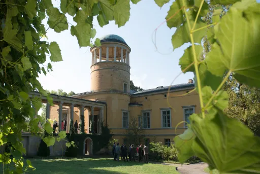 Yellow observatory building framed by green leaves, people gathered near the entrance.