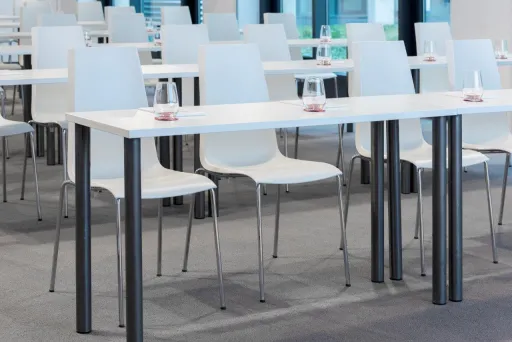 Helle Seminarraumreihe mit weißen Stühlen und Tischen, Wassergläser bereitgestellt.