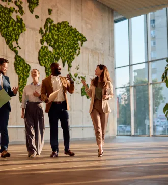 Four business professionals walking and chatting in a modern office with world map wall décor.