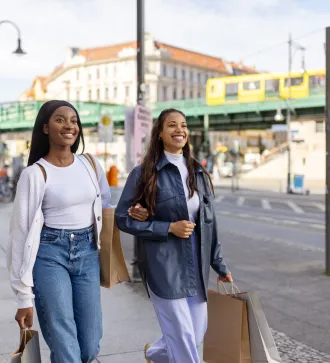 Zwei afrikanische Frauen mit Einkaufstaschen, die die Straße hinuntergehen. Freundinnen beim Einkaufen in der Stadt.