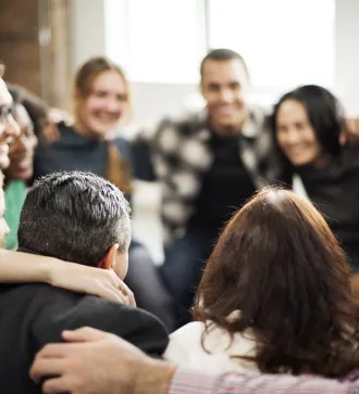 Mehrere Menschen sitzen lachend im Kreis und umarmen sich.