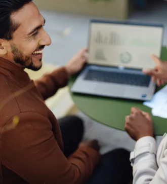Two people talking, one pointing to diagrams on a laptop screen