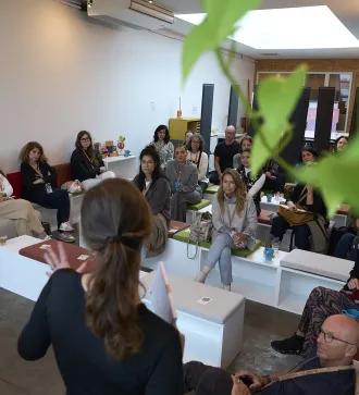 A woman stands in front of a group of participants and speaks.
