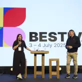 Zwei Speaker stehen auf der Bühne des BESTIVAL 2025 in Berlin. Im Hintergrund sind das Event-Logo und das Veranstaltungsdatum „3–4 July 2025“ groß zu sehen. Eine Frau spricht ins Mikrofon, ein Mann hört zu.