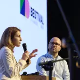Zwei Speaker im Gespräch auf der Bühne des BESTIVAL 2025 in Berlin. Eine Frau spricht ins Mikrofon, ein Mann hört aufmerksam zu. Im Hintergrund ist das BESTIVAL-Logo sichtbar.