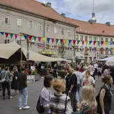 Buntes Treiben im Innenhof der Alten Münze in Berlin während des BESTIVAL 2025. Menschen schlendern zwischen Foodständen, Zelten und bunten Wimpelketten – im Hintergrund ist der Berliner Fernsehturm zu sehen. Sommerliche Festivalatmosphäre.